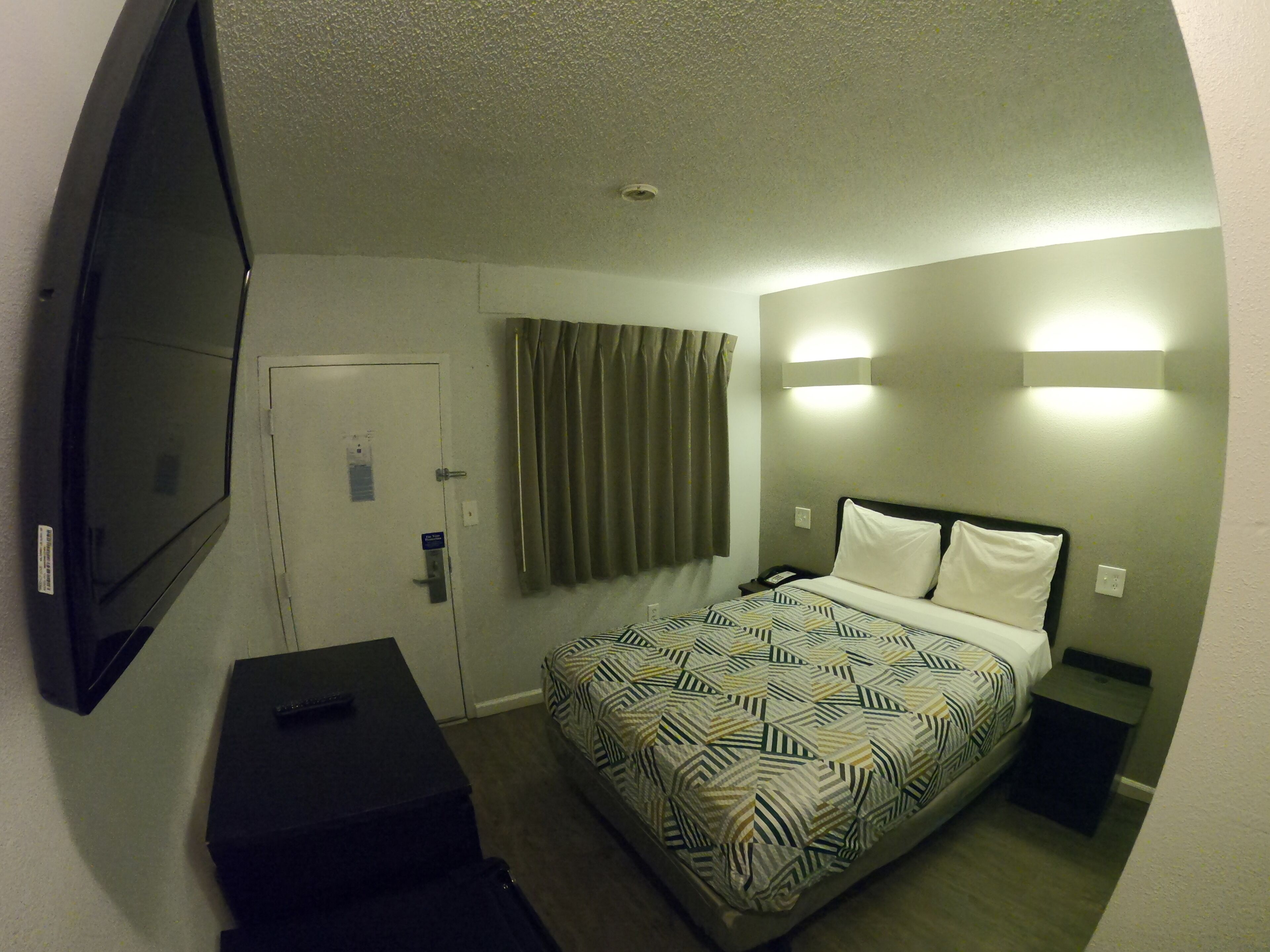 Een hotelkamer met een bed, een televisie, een bureau en een deur.