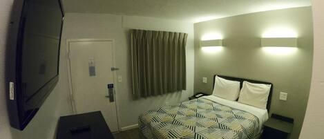 Quarto de hotel com cama, televisão, escrivaninha e porta.