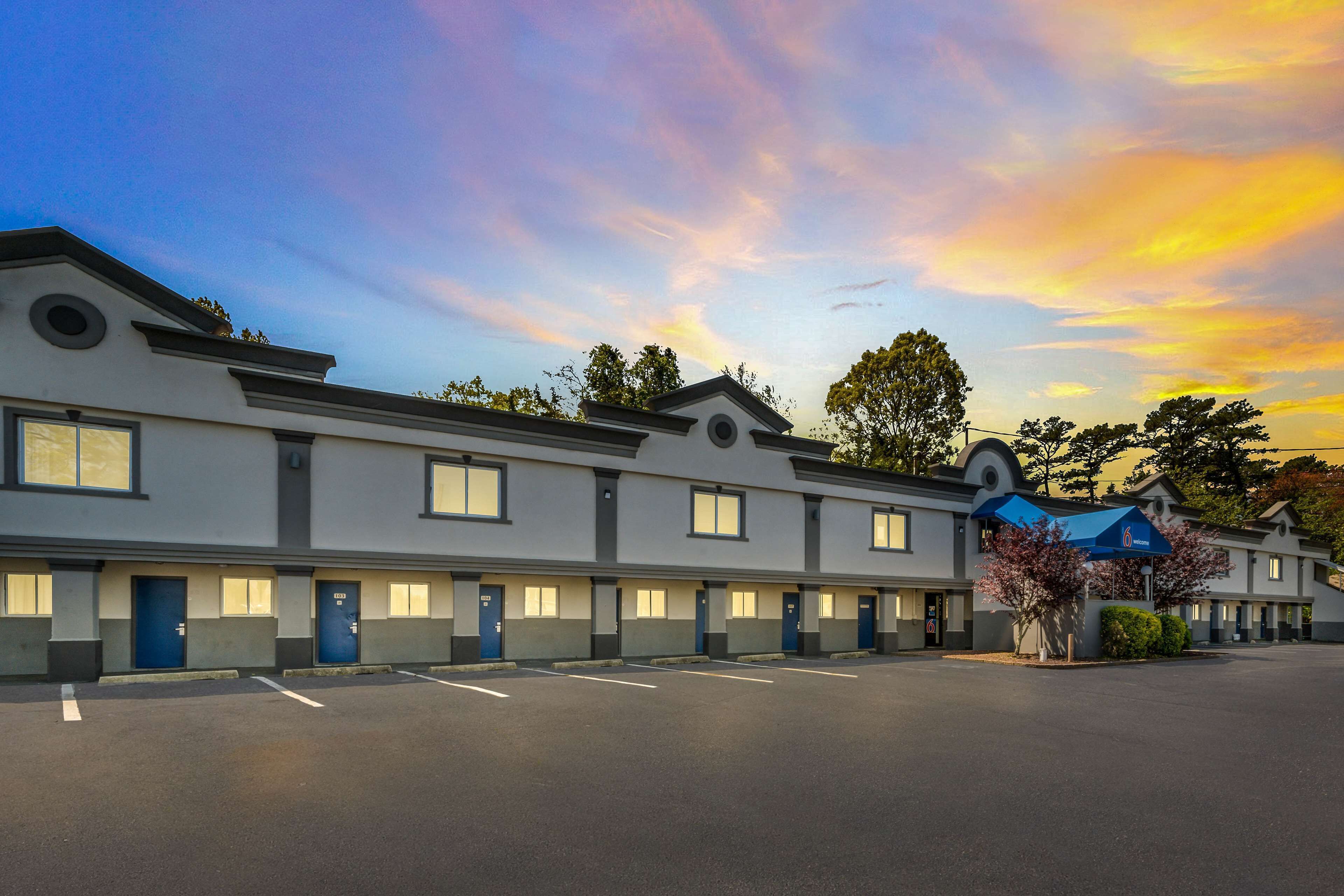A motel with a row of rooms, a parking lot, and a clear sky with clouds.