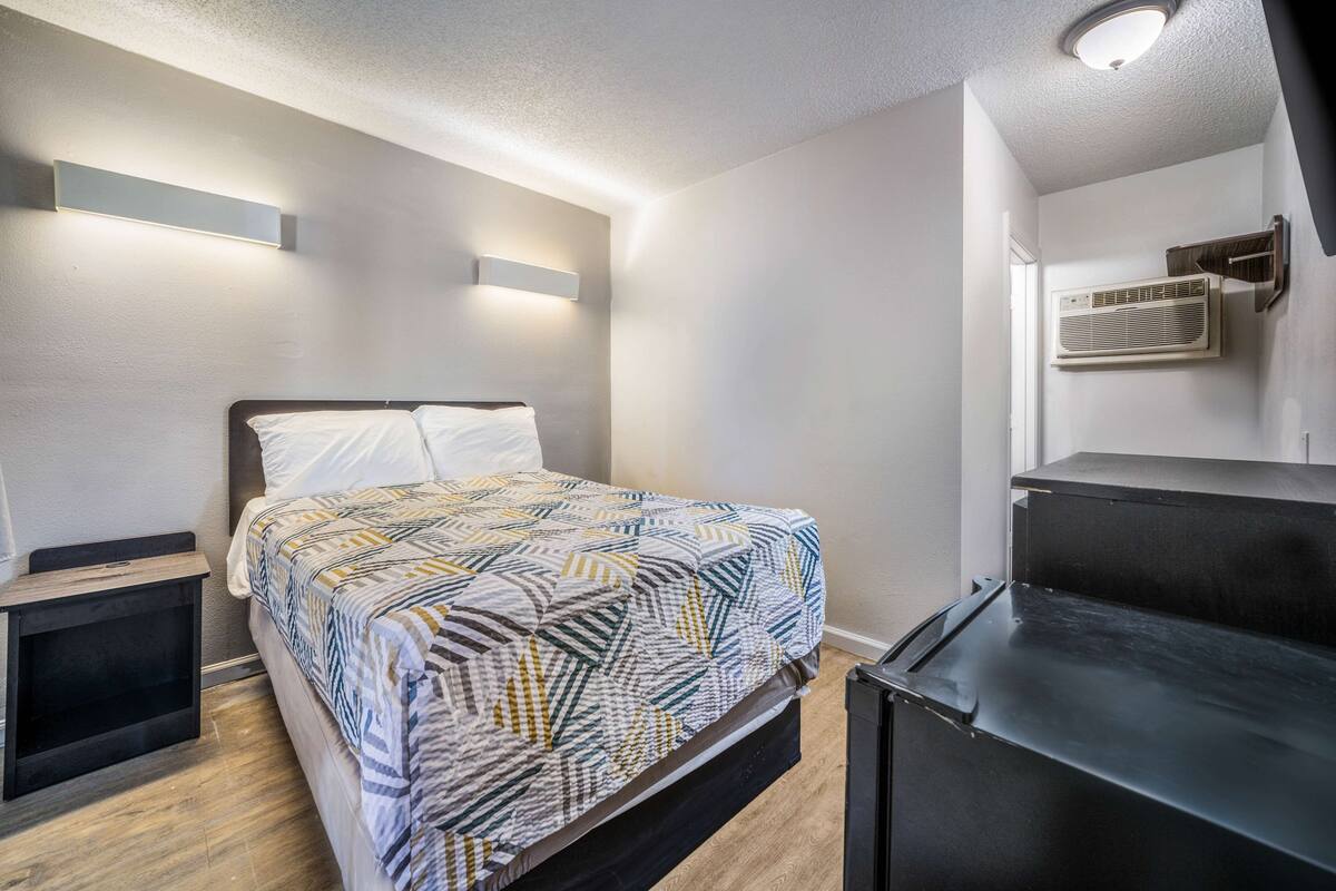 Un dormitorio con cama, mesitas de noche, aire acondicionado en la pared y una lámpara de techo.