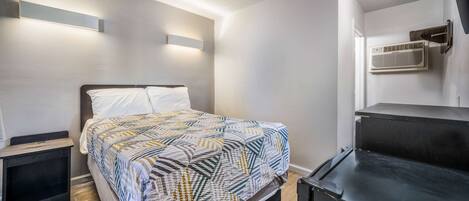 A bedroom with a bed, bedside tables, a wall-mounted air conditioner, and a ceiling light.