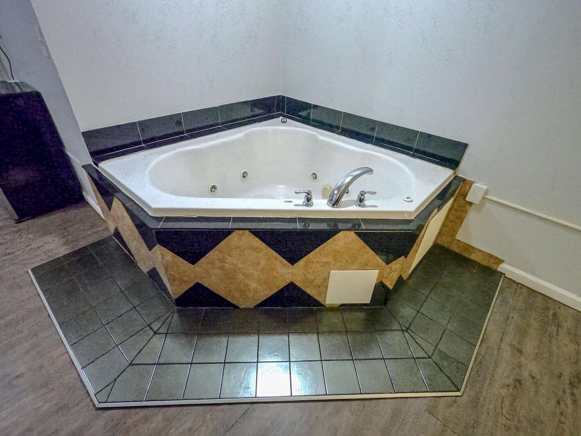 A corner bathtub with a black and beige tile design, a white sink, and a chrome faucet.