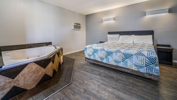 A modern bedroom with a large bed, a separate bathtub, and a small bedside table. - Motel 6 Toms River, NJ - Near Seaside Heights (Toms River)