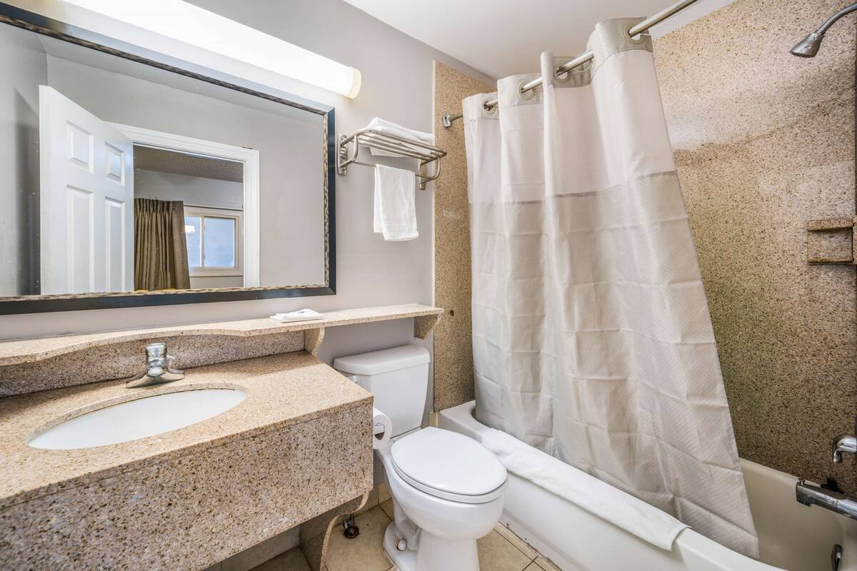 Un baño con lavamanos de granito, inodoro, bañera y cortina de ducha.