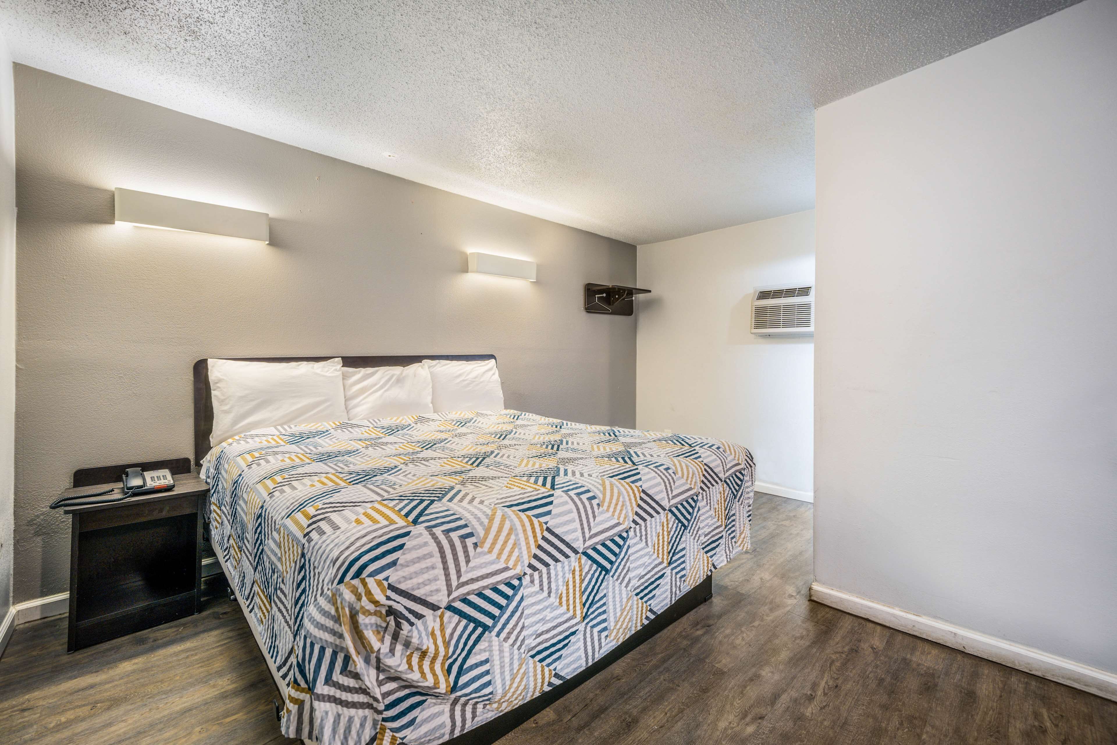 Un dormitorio con cama, mesitas de noche, luces fijadas a la pared y un equipo de aire acondicionado.