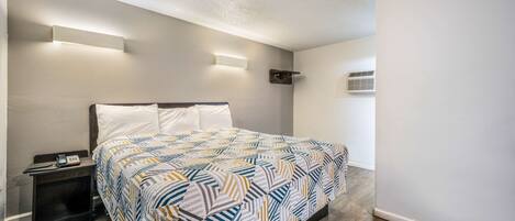 Un dormitorio con cama, mesitas de noche, luces fijadas a la pared y un equipo de aire acondicionado.