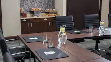 Un salón de conferencias con una larga mesa, sillas negras y una pequeña kitchenette al fondo.