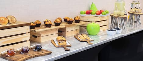 Une table de buffet proposant une variété de produits de boulangerie, de fruits et de boissons.