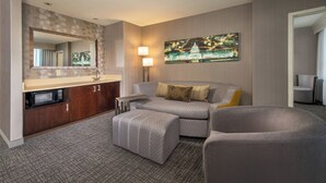 Habitación de hotel con kitchenette, un sofá, una silla, un espejo grande y un cuadro colgado en la pared.