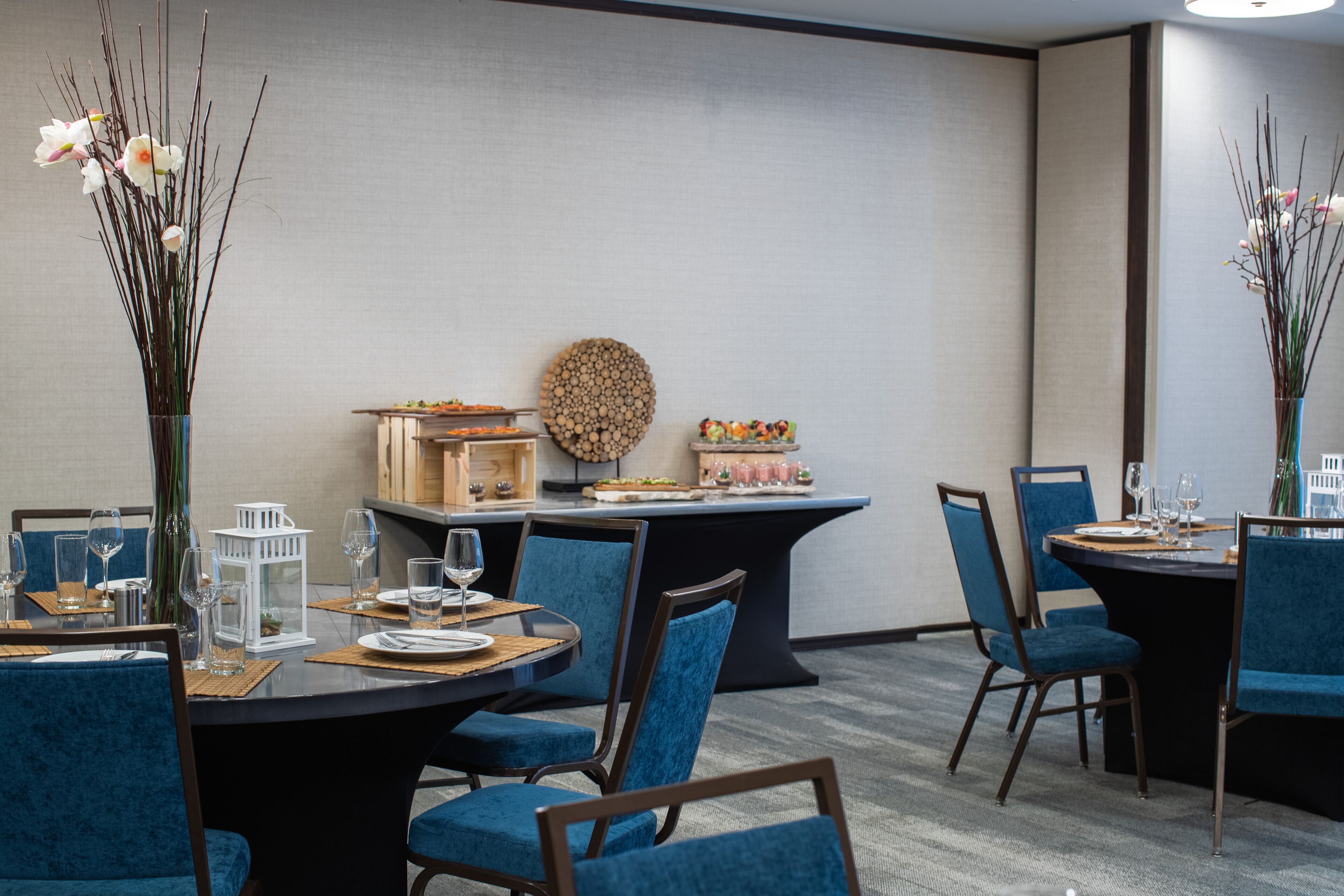 A dining area with round tables, blue upholstered chairs, and a buffet setup.