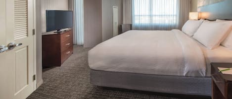A hotel room with a large bed, a TV on a wooden dresser, and a view of the outdoors through the window.