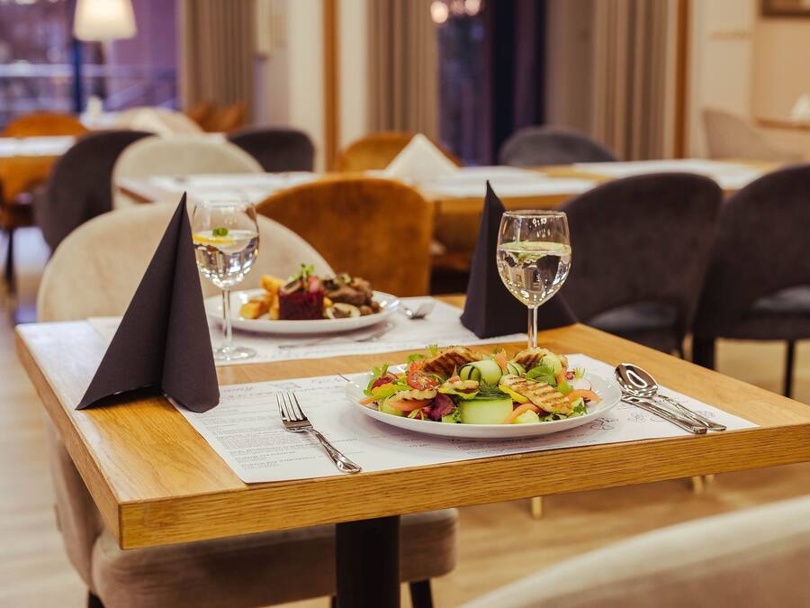 Un restaurante con una mesa lista para comer, que incluye un plato de ensalada, una copa de vino blanco y un menú.