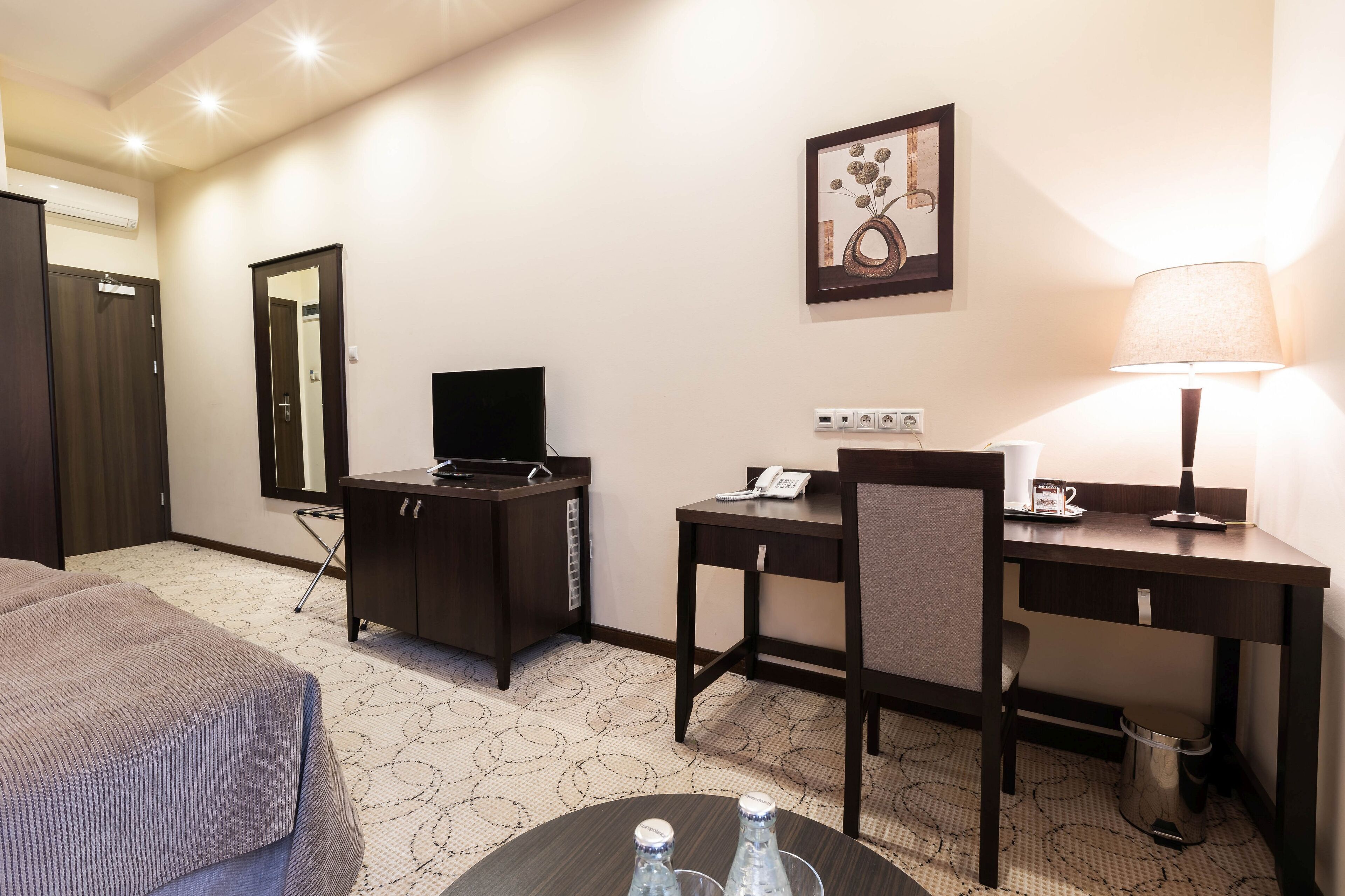Una habitación de hotel con una cama, un escritorio, una silla, un televisor, una lámpara y un cuadro en la pared.