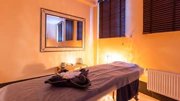 A massage table with towels and a small table with a lamp and a glass object.