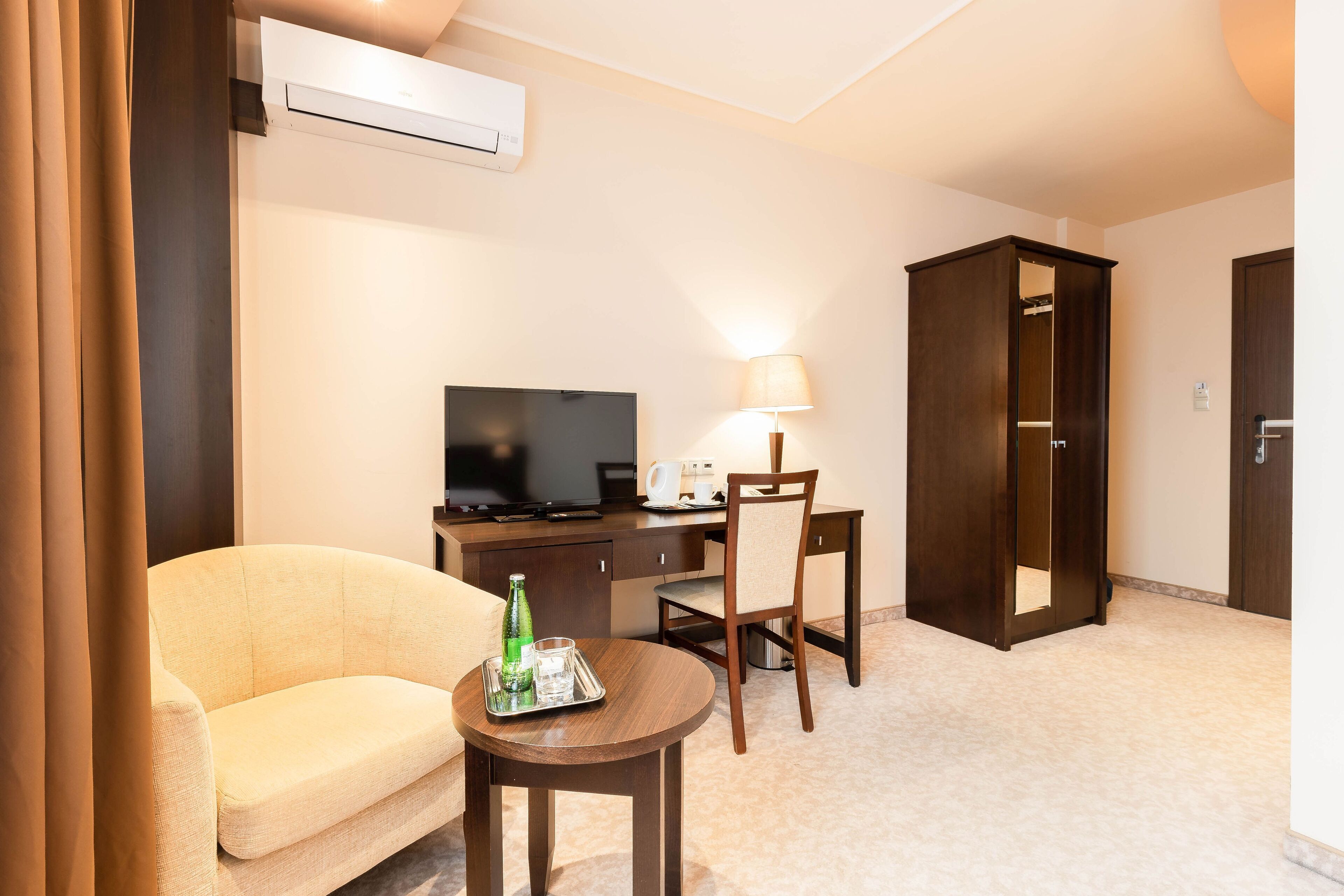 Una habitación de hotel con sofá, escritorio con computadora, televisor, lámpara y armario.