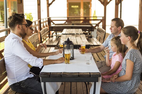 Una familia de cuatro personas sentada en una mesa de madera con un farol, disfrutando de bebidas en un espacio al aire libre.
