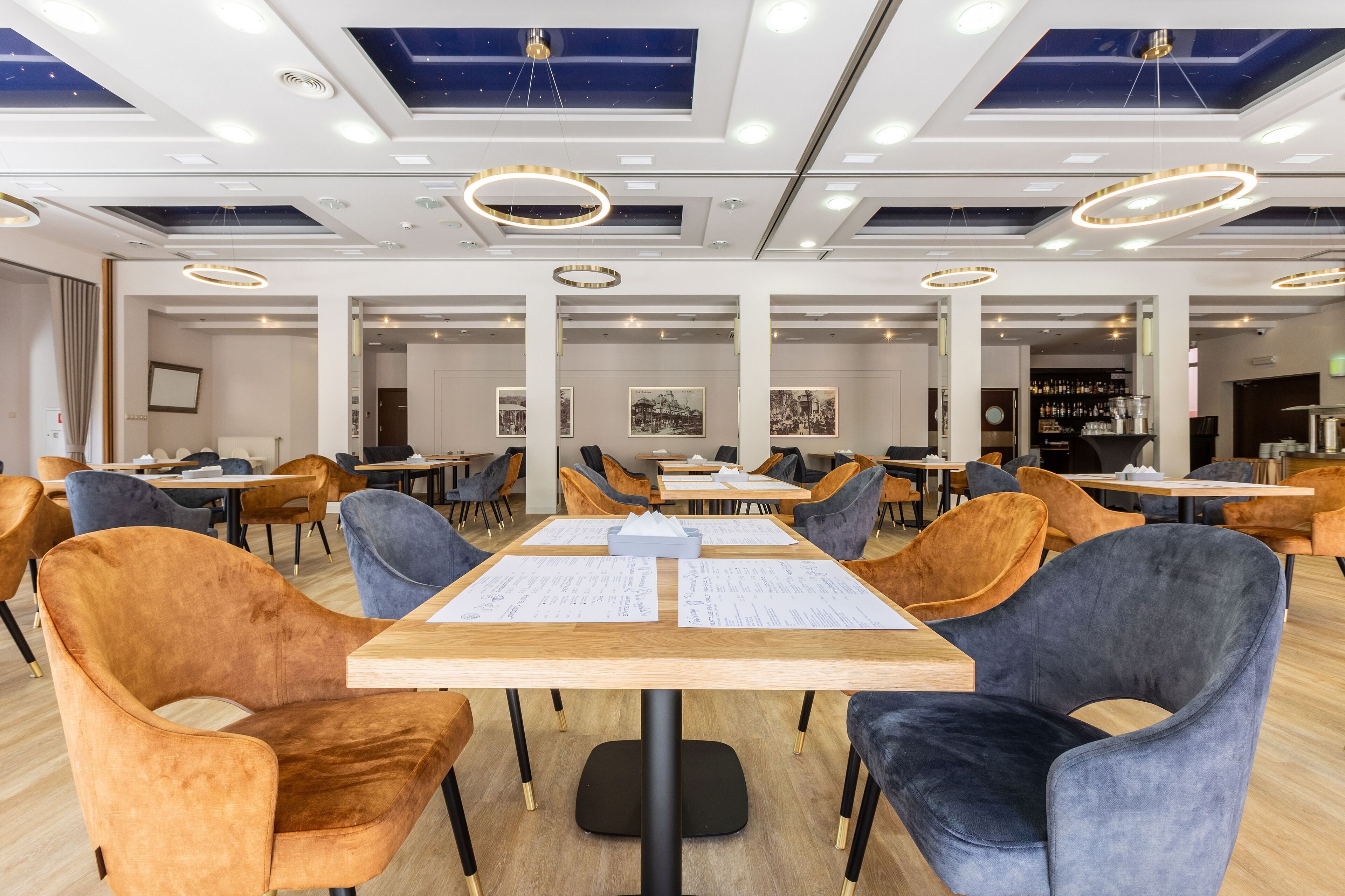 A modern dining area with tables and chairs, ceiling lights, and framed pictures on the walls.
