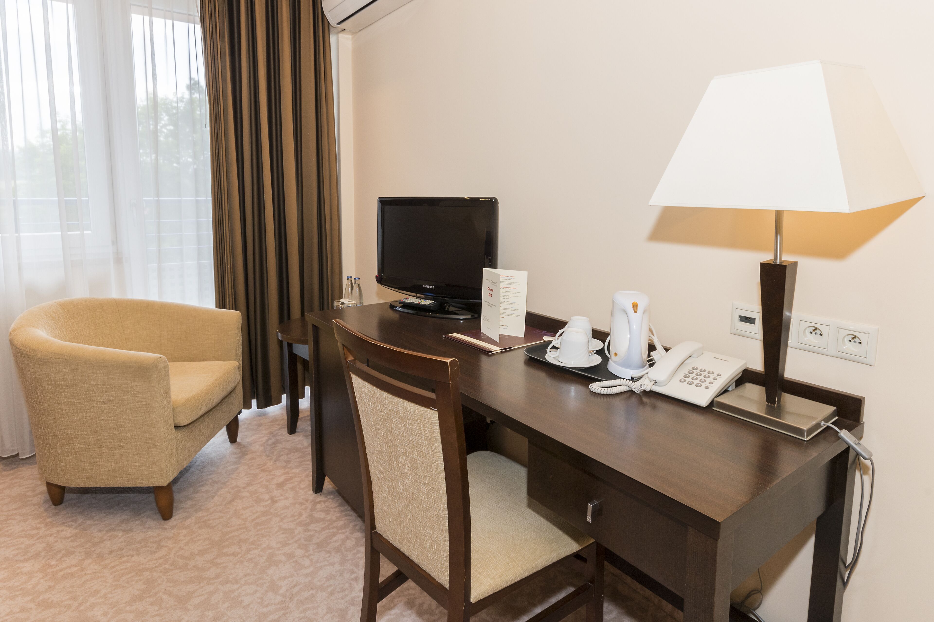 Una habitación de hotel con un escritorio de madera, un televisor, una lámpara, un teléfono y una silla.