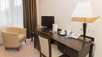 Una habitación de hotel con un escritorio de madera, un televisor, una lámpara, un teléfono y una silla.