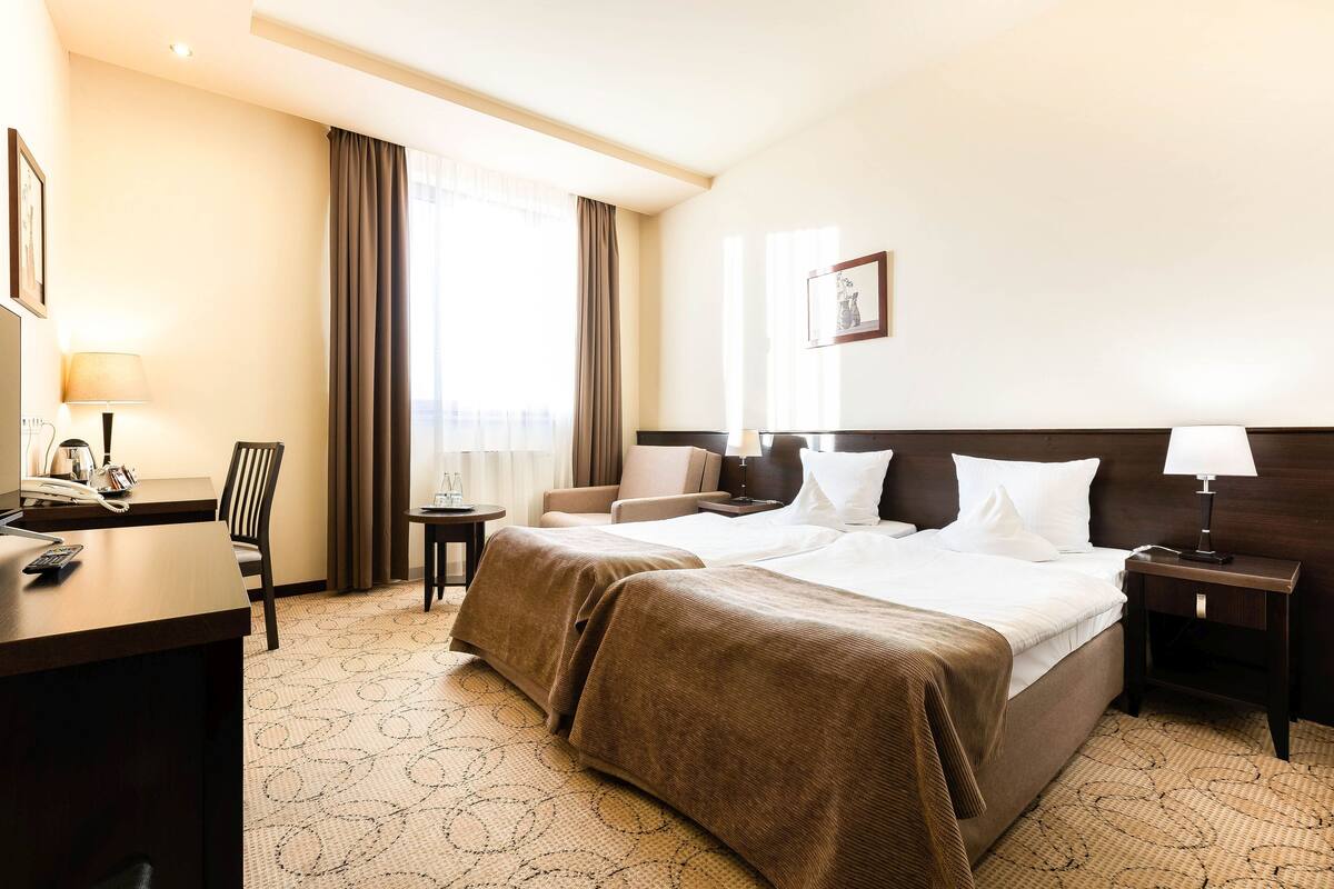 A hotel room with a large bed, a desk with a telephone, a chair, and a small table.