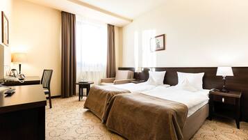 A hotel room with a large bed, a desk with a telephone, a chair, and a small table.
