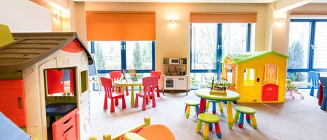 Un cuarto de juegos infantil, lleno de color, con una casita, mesas, sillas y una zona de cocina.