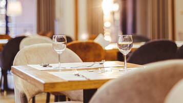 A restaurant with a wooden table, two wine glasses, and a modern chandelier.
