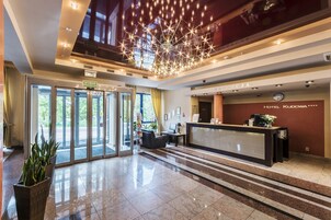 Vestíbulo de hotel con mostrador de recepción, una lámpara moderna y entrada de vidrio.