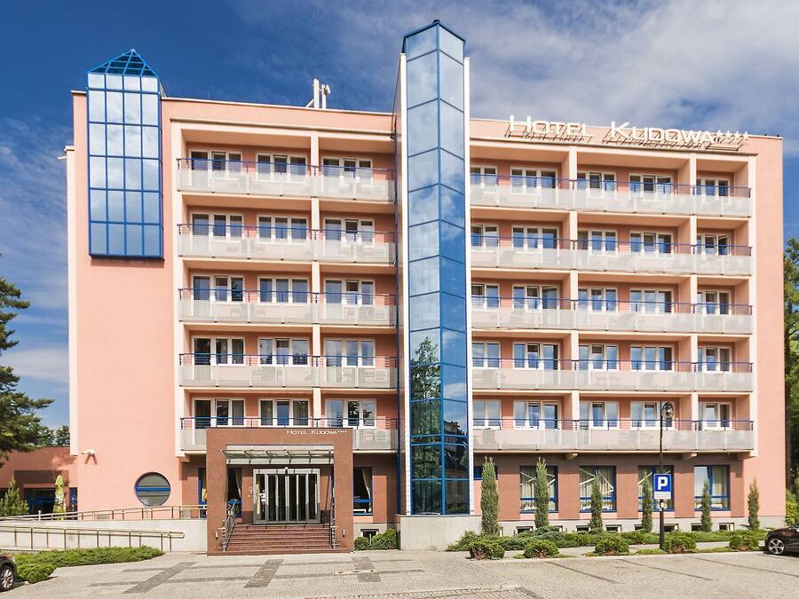 Un hotel de varios pisos con una torre central de vidrio, balcones en cada planta y cielo despejado.
