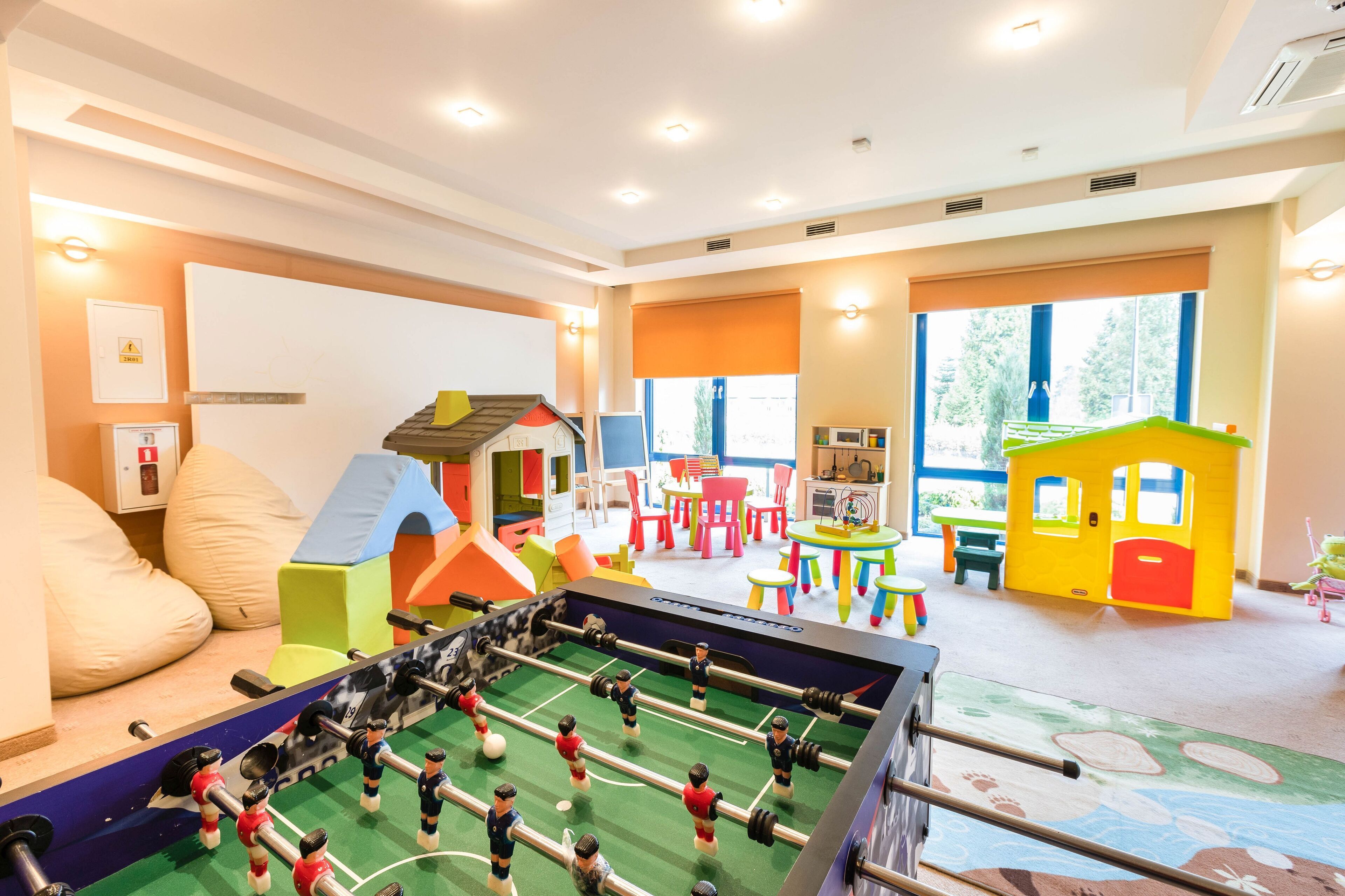 A children's playroom with a foosball table, colorful play structures, and large windows.