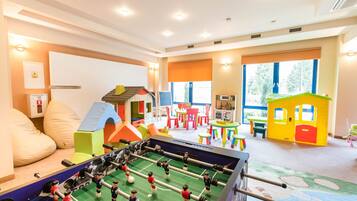 A children's playroom with a foosball table, colorful play structures, and large windows.