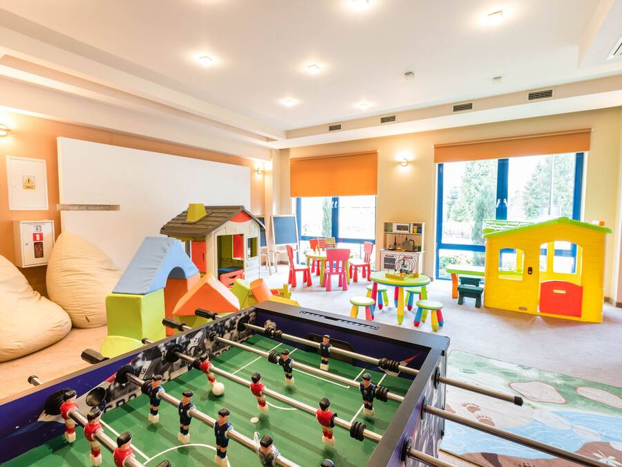 Une salle de jeux pour enfants avec un baby-foot, des structures de jeu colorées et de grandes fenêtres.