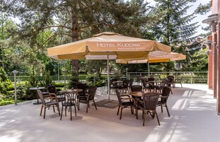 Un área de estar al aire libre con mesas y sillas, cubierta por sombrillas con la etiqueta "Hotel Kudowa".