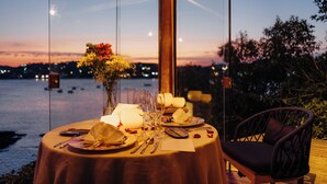 A table set for a meal with a view of the water and city lights at dusk.