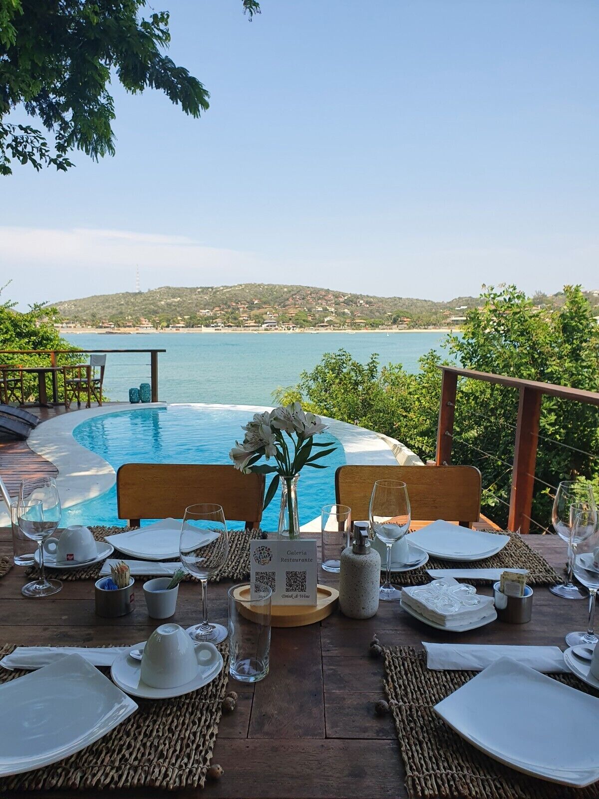 A dining table set for two with a view of a pool and the sea.