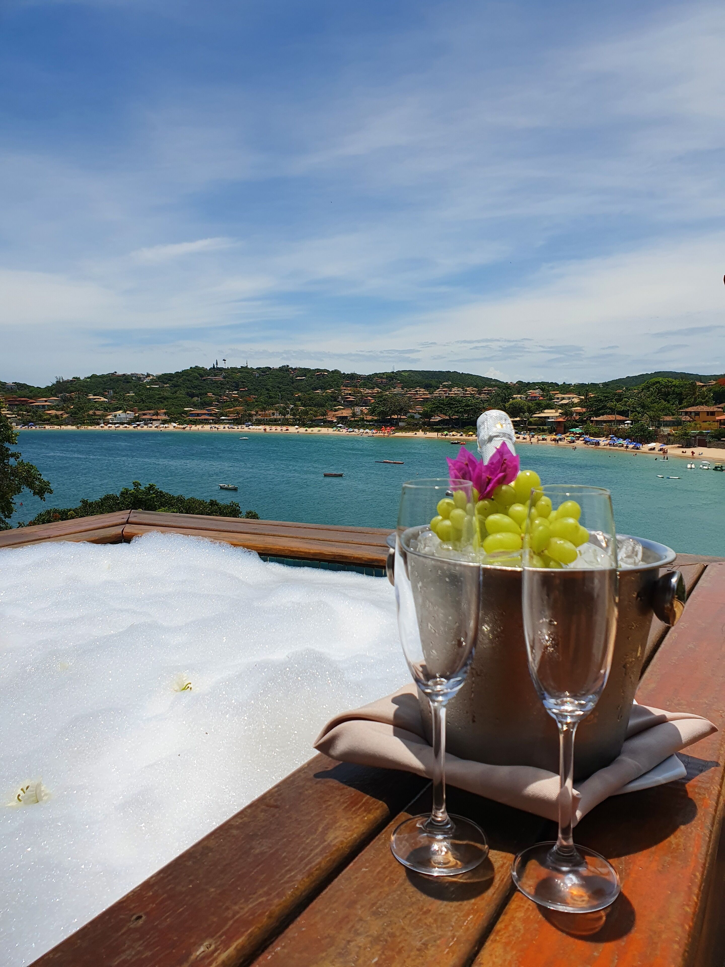 A wooden table with a champagne bucket containing a glass of champagne and a glass of water, with a view of a beach and ocean in the background.
