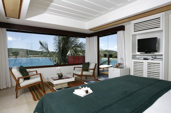 A modern hotel room with a large bed, two chairs, a small table with a vase, and a TV on a white cabinet. - Insolito Boutique Hotel (Búzios)