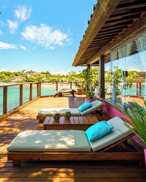 A wooden deck with lounge chairs and a glass railing overlooking a beach.