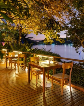 Un espace de restauration en plein air, avec des tables et des chaises en bois, donnant sur un lac paisible au crépuscule.