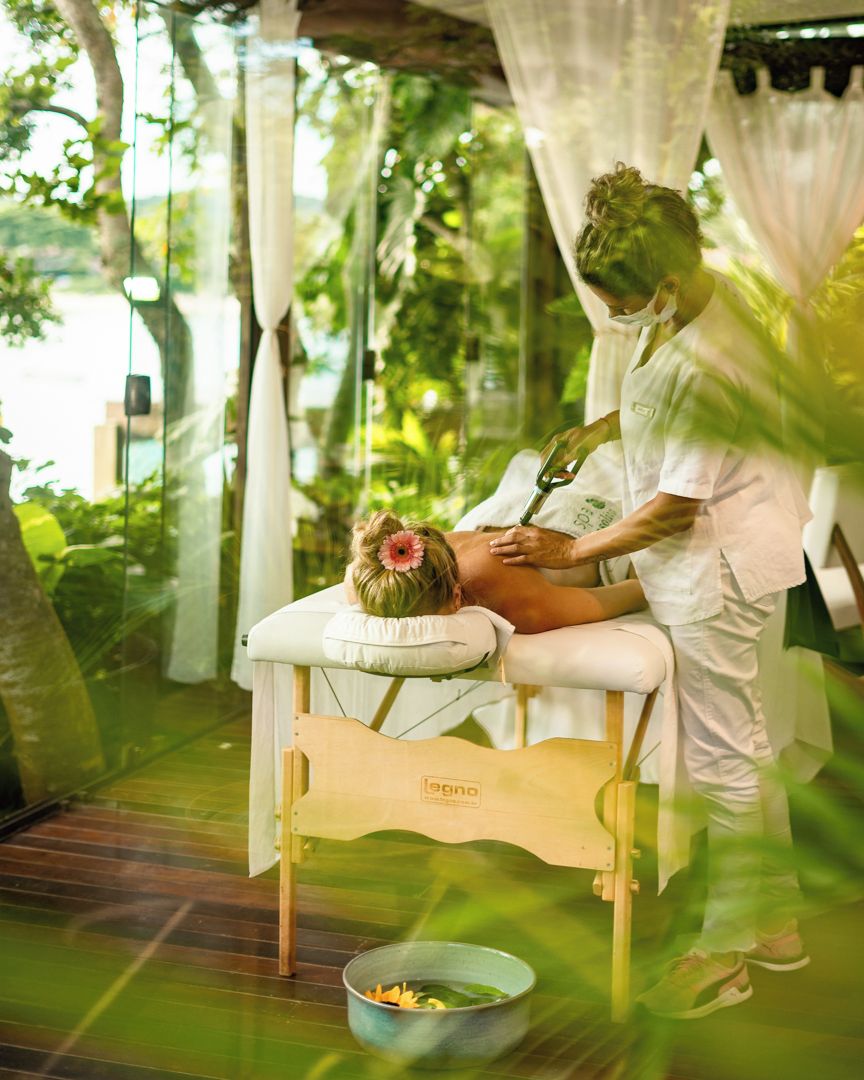 A massage therapy session in a room with a wooden massage table, a bowl of fruits, and a curtain backdrop.