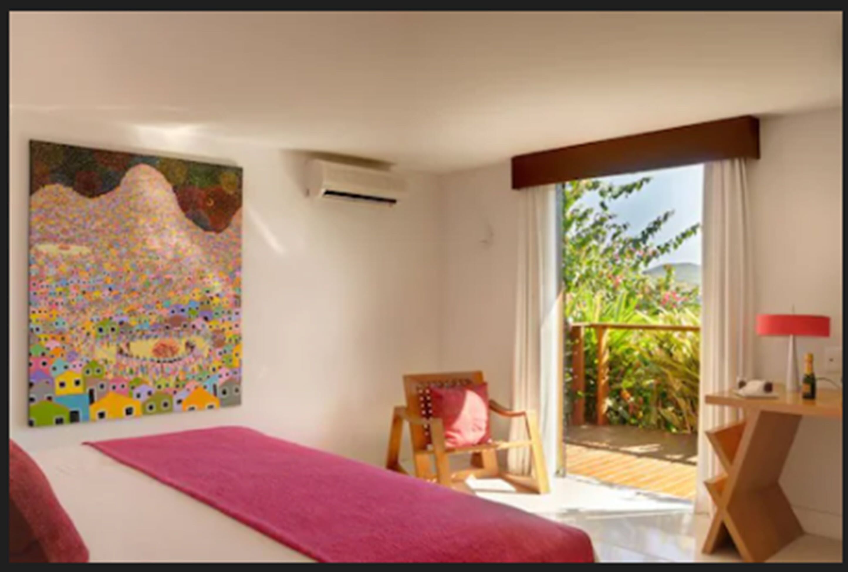 Habitación de hotel con cama, una silla, un escritorio y un balcón con vistas a la vegetación.