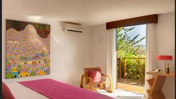 Habitación de hotel con cama, una silla, un escritorio y un balcón con vistas a la vegetación.