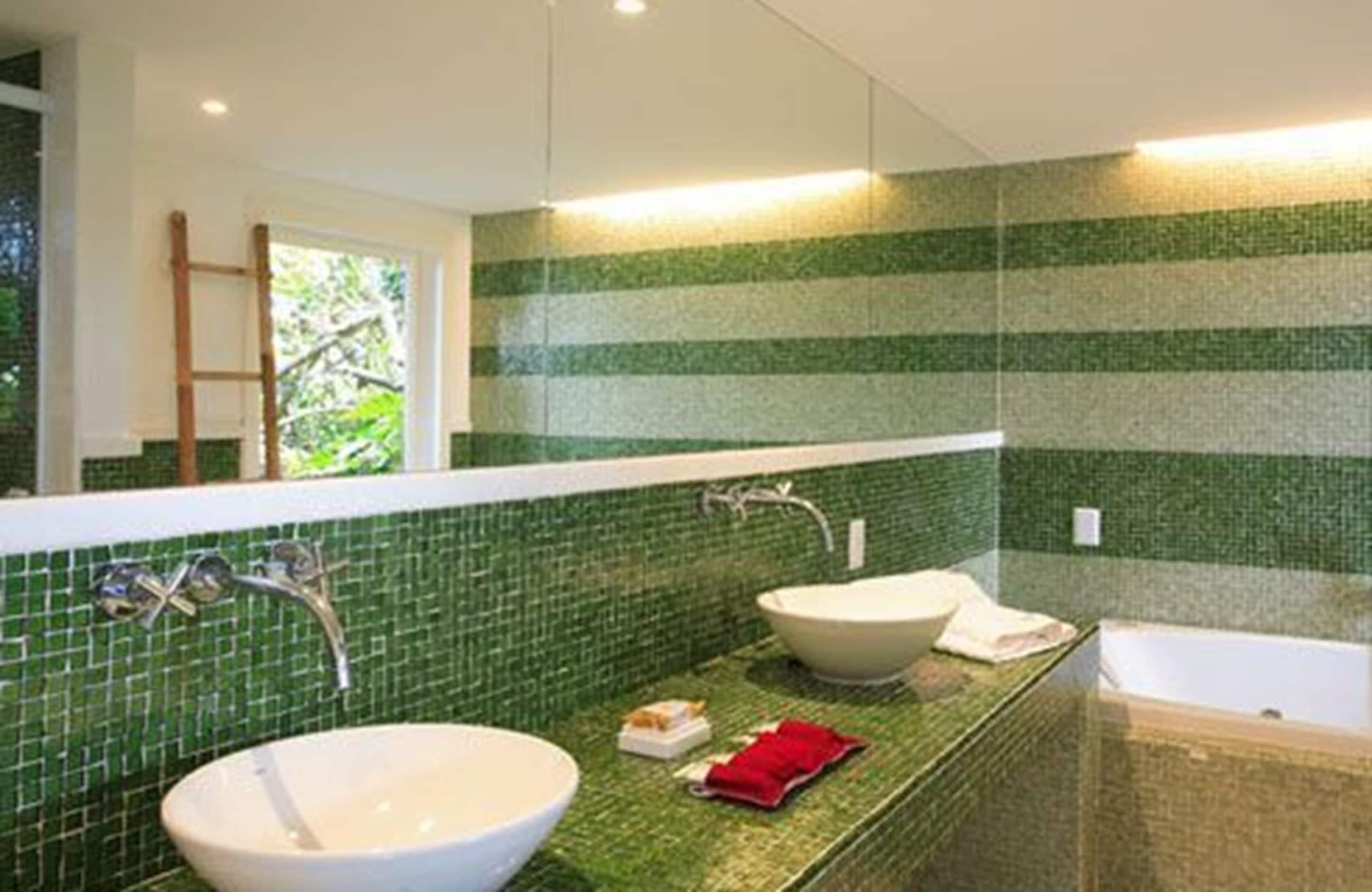 A bathroom with a green mosaic wall, a large sink, a bathtub, and a mirror.