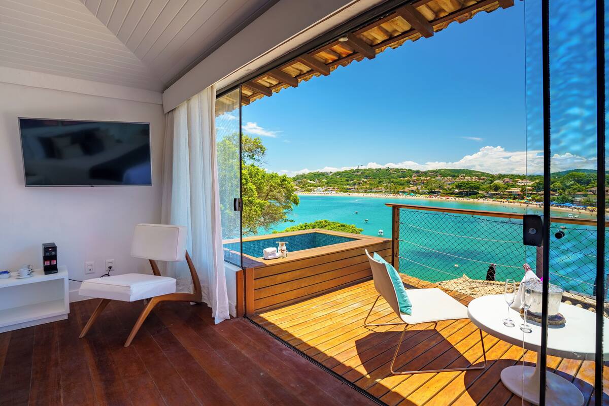 Ein Balkon mit Holzboden, einem kleinen Tisch mit einem Glas Wasser, einem Stuhl und einem an der Wand befestigten Fernseher.