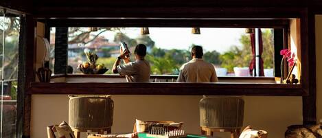 A room with a pool table, wooden chairs, a large window with a view, and a ceiling fan.