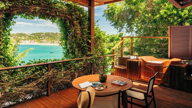 A wooden deck with a round table, chairs, and a hot tub.