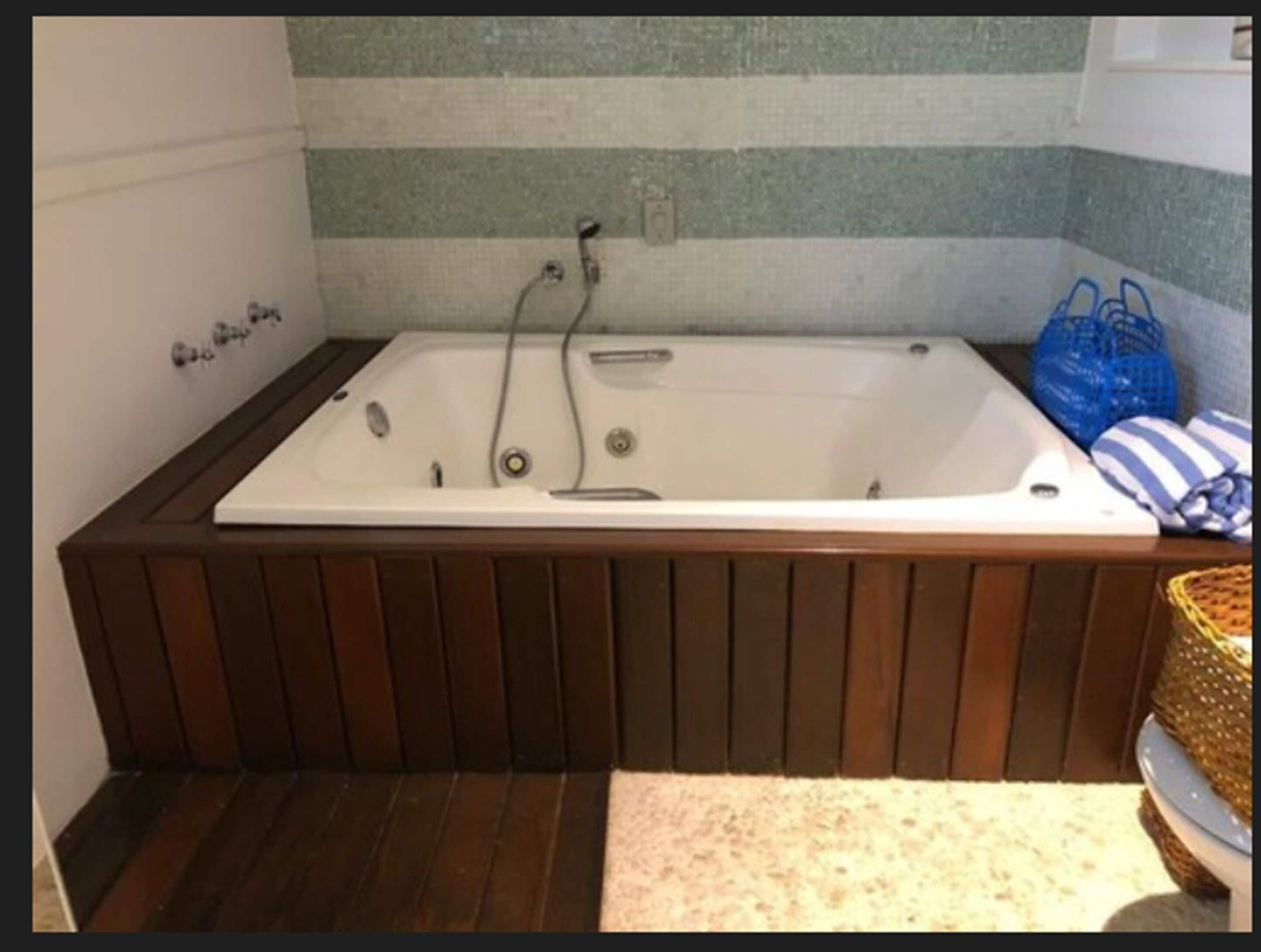 Un baño con piso de madera, una bañera blanca y una pared a rayas.