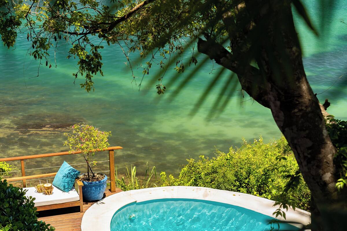 Ein Schwimmbecken mit Holzterrasse, Liegestühlen und Blick auf ein Gewässer.