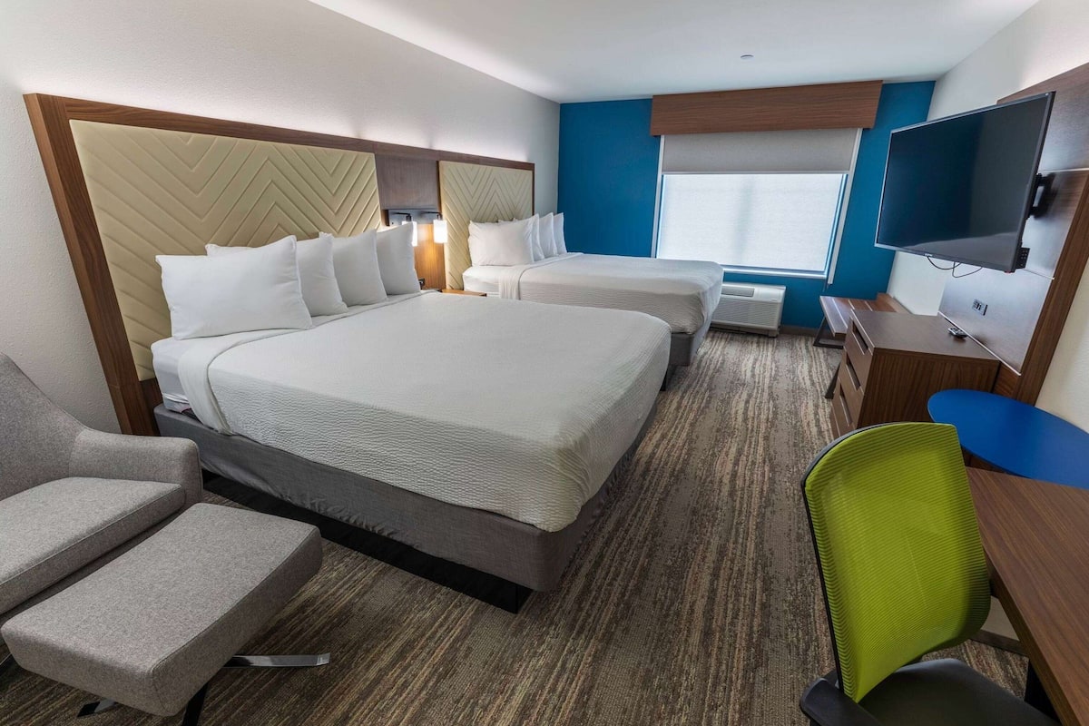 Una habitación de hotel con dos camas, televisión, escritorio y silla.