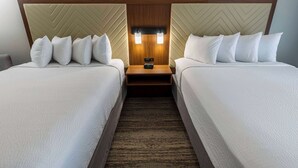 Une chambre d’hôtel avec deux lits, une tête de lit en bois, une table de chevet avec une horloge et un sol recouvert de moquette.